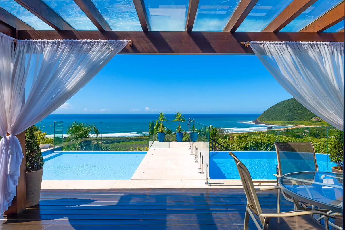 Piscina infinita de Morada Prainha, vista desde la pérgola con cortinas blancas, con el mar de Praia do Silveira al fondo