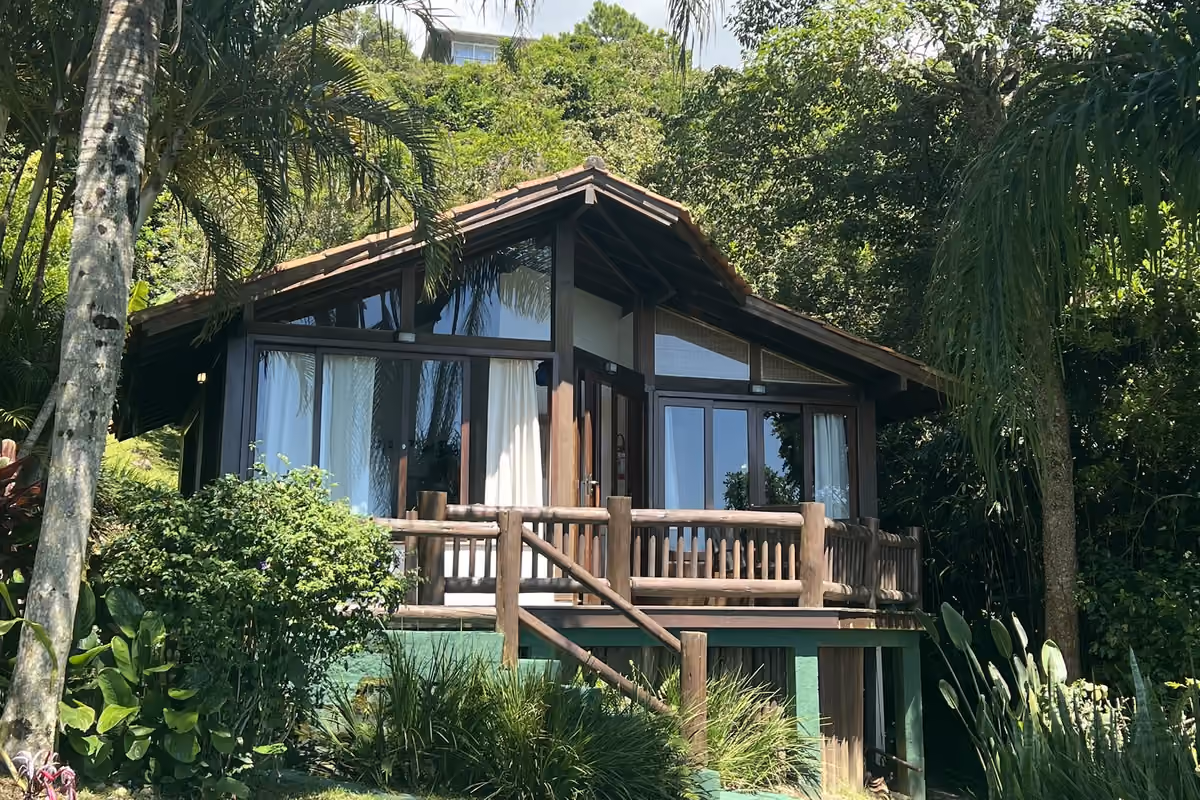 Casa de madera de Moradas da Silveira con balcón, rodeado de palmeras y vegetación