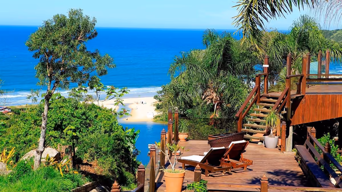 Deck de madeira com espreguiçadeiras da Pousada Descanso do Rei, com vista para a lagoa e o mar da Praia do Rosa