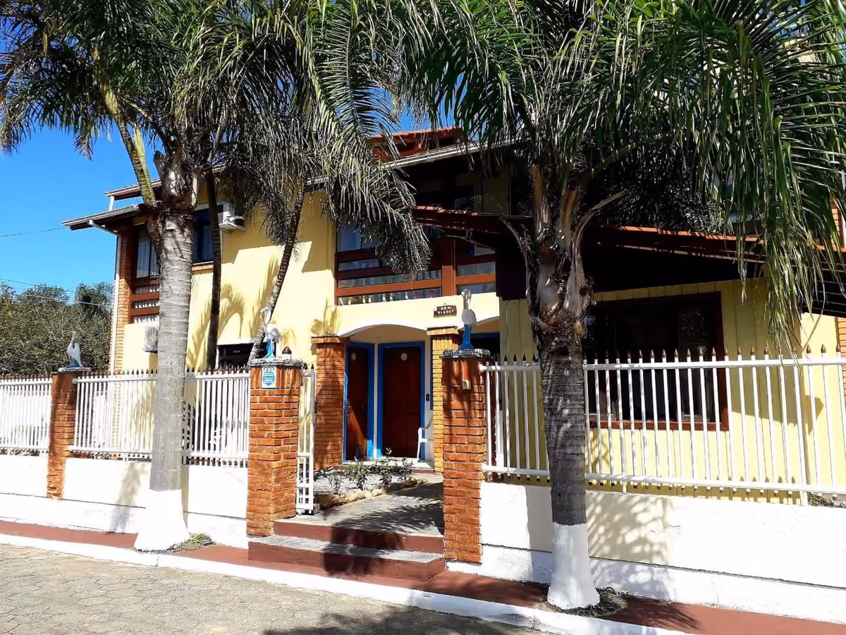 Fachada amarela da Pousada Estrela Mares, na Guarda do Embaú, com palmeiras e jardim na frente