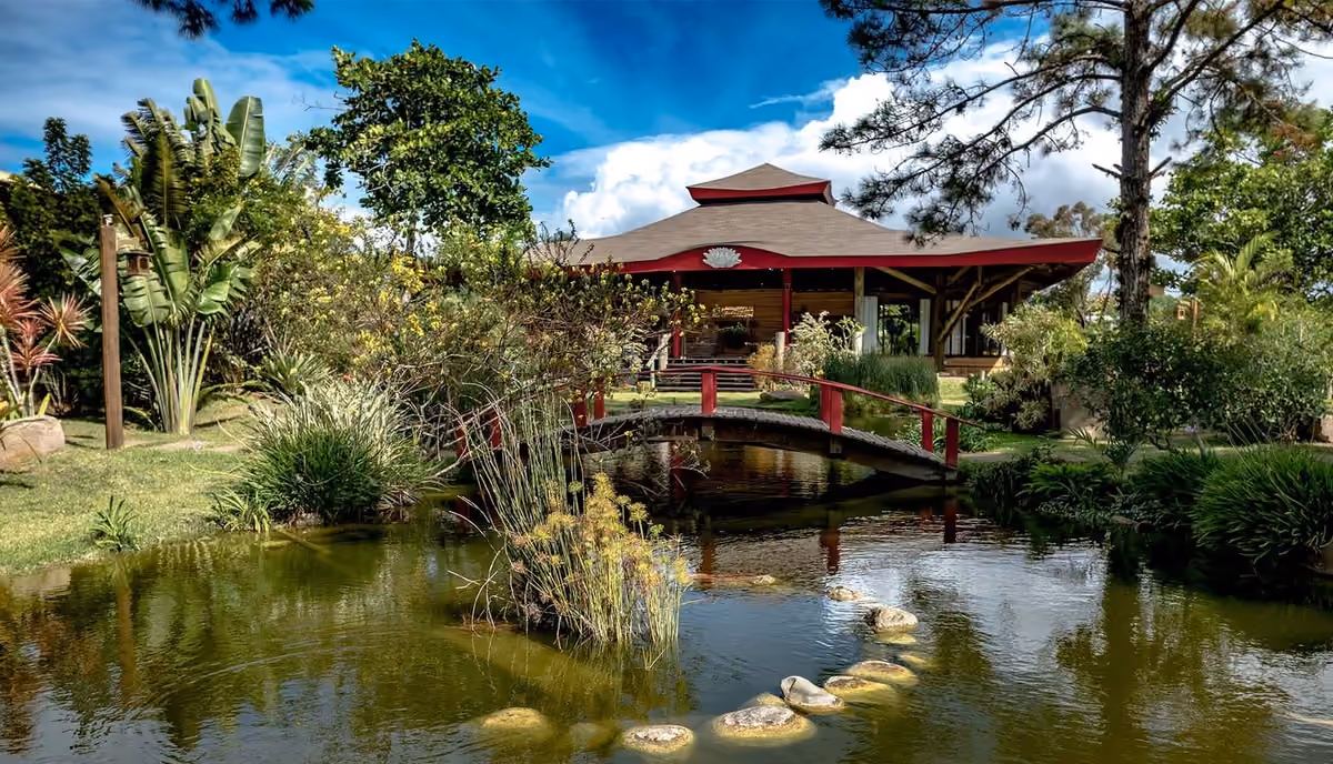 Jardim com lago, ponte vermelha e templo da Pousada Mevlana Garden, na Barra de Ibiraquera, perto da Praia do Rosa