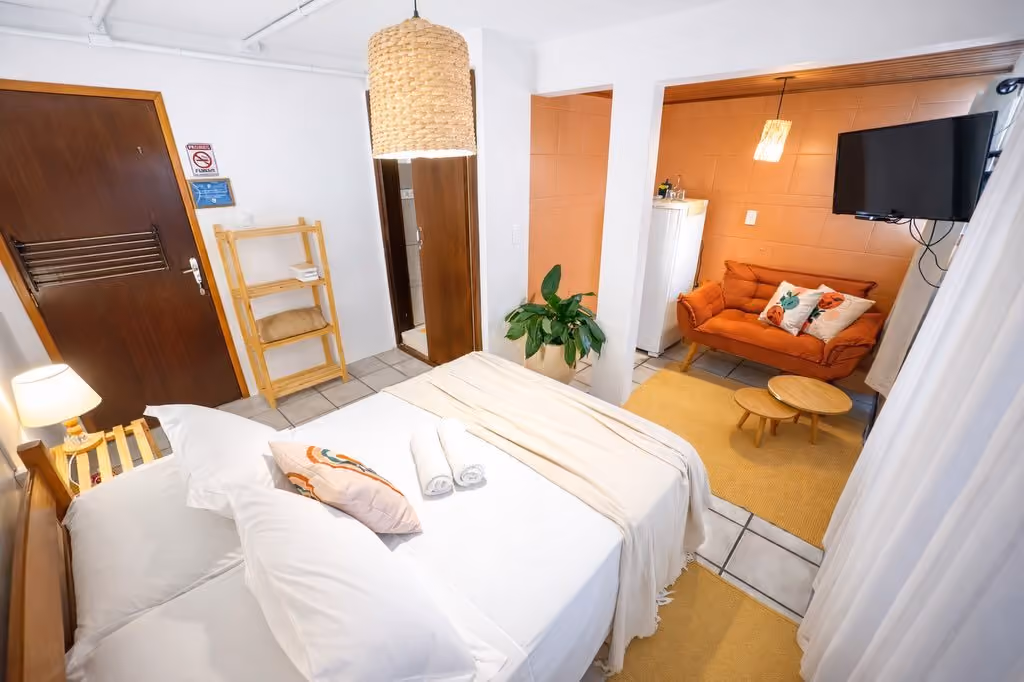 Suíte da Pousada Surf na Guarda, na Guarda do Embaú, com cama de casal e saleta com sofá laranja