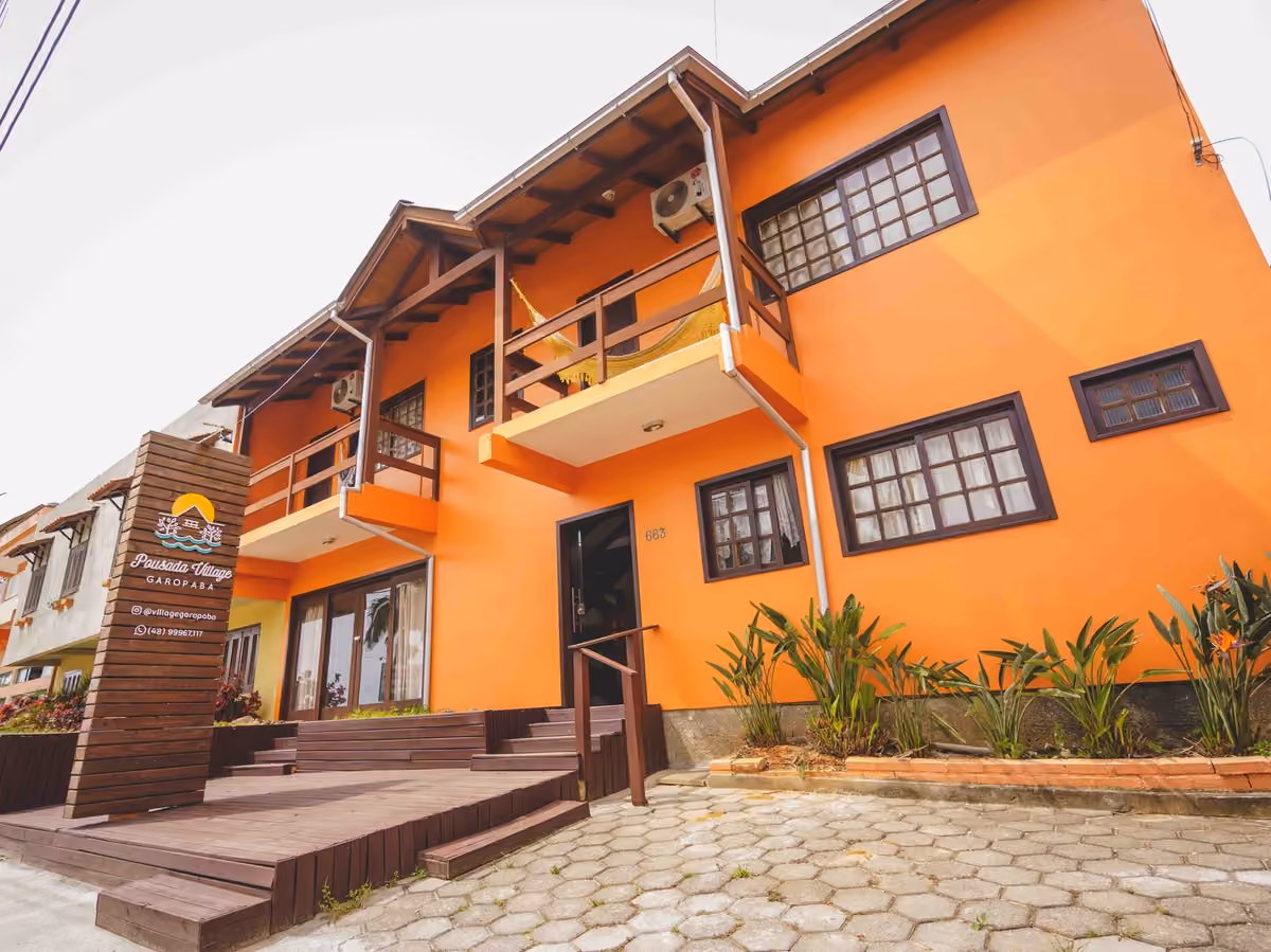 Fachada laranja da Pousada Village Garopaba, no centro de Garopaba, com varandas de madeira e deck de entrada