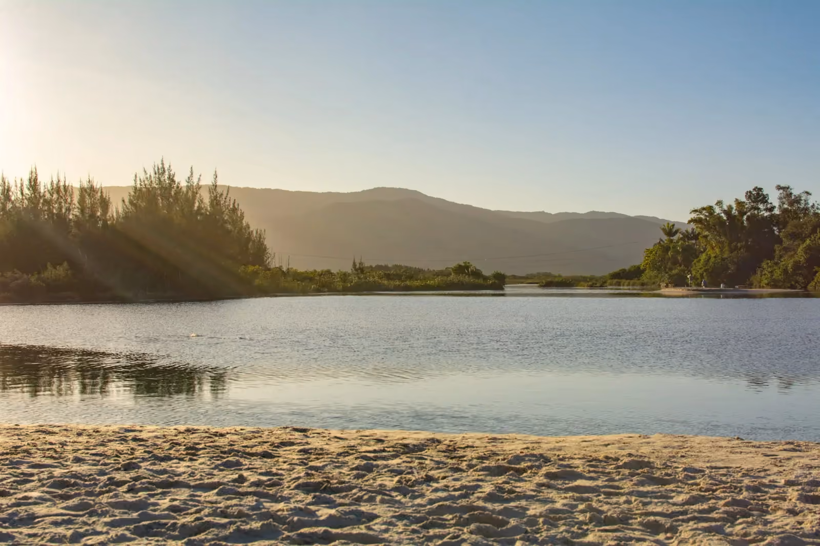 Canal de agua quieta en la Praia da Barra, con franja de arena y morros al fondo