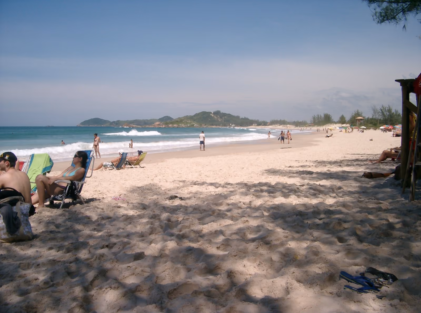 Franja ancha de arena de la Praia da Ferrugem, con gente en reposeras y el morro al final de la playa