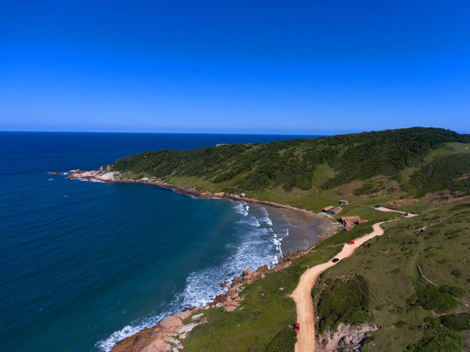 Ponta sul do Rosa vista de drone, com a estrada de terra, o costão e o mar azul
