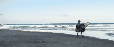 Surfista caminhando com a prancha pela areia do Rosa Norte, com o mar ao fundo