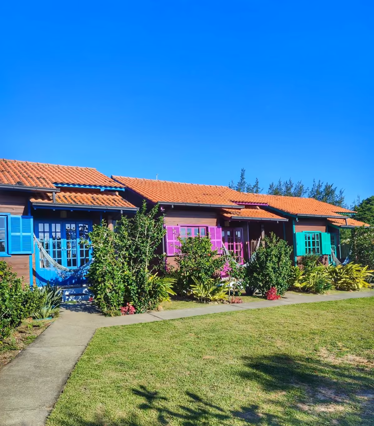 Cabanas de madeira coloridas do Prana Guest House, com gramado e jardim na frente