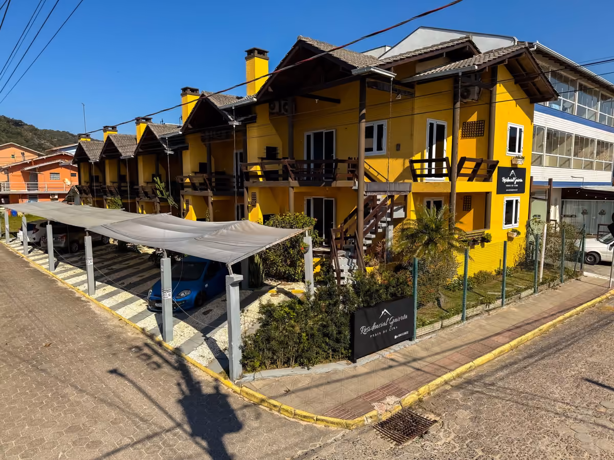Fachada amarela do Residencial Gaivota, na Praia de Cima, com varandas de madeira