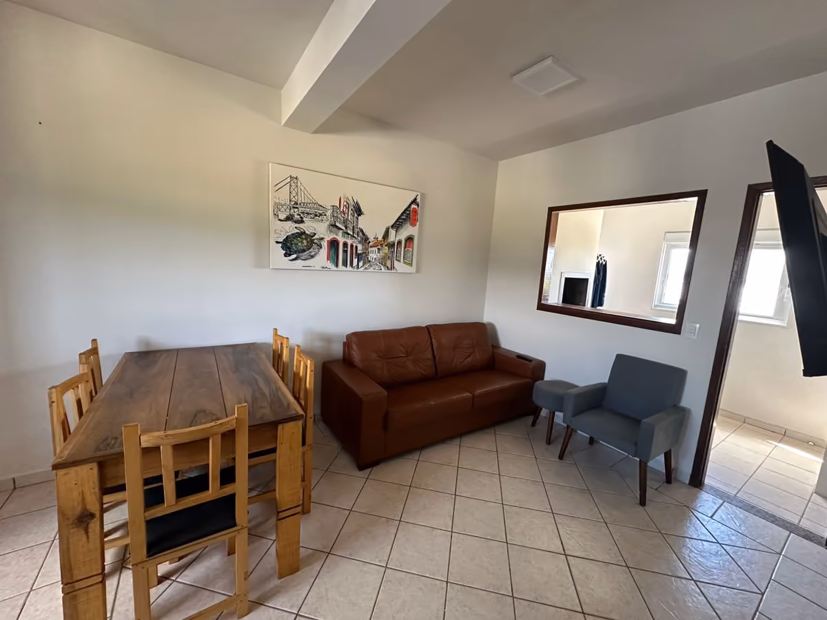 Sala do apartamento da Villa Cavaliere, na Praia da Pinheira, com mesa de jantar e sofá